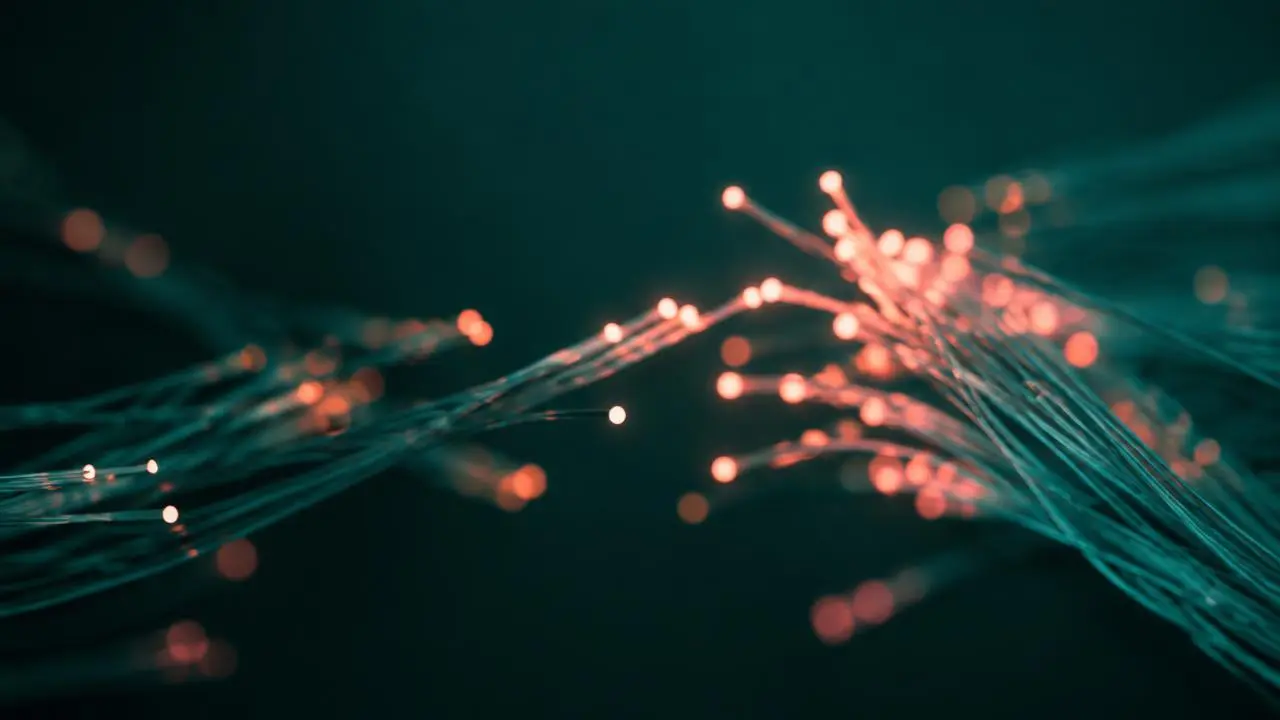 Glowing teal and coral fiber optic strands reaching toward each other, symbolizing connection